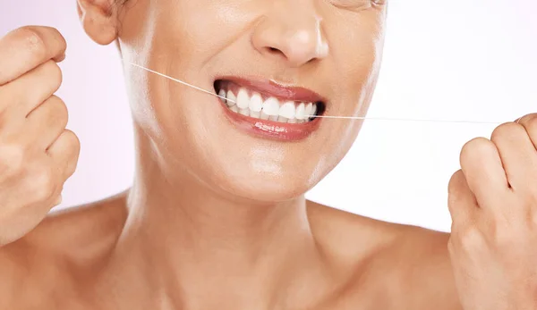 紫色の背景に隔離されたスタジオでの掃除 または歯のケアのための歯を流れる顔 笑顔と女性 口腔健康 化粧品 健康のための歯科フロスと幸せな成熟した女性モデル — ストック写真