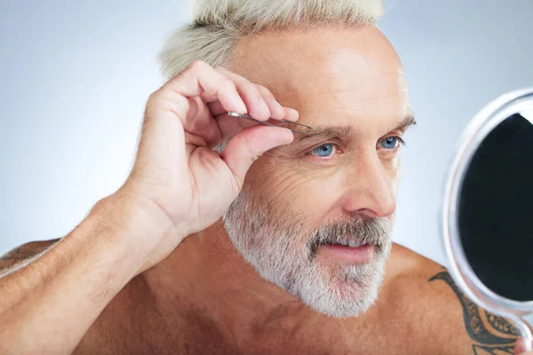 Stock image Senior man, bathroom tweezers and mirror check in a studio doing hair removal and grooming. Wellness, eyebrows and beauty routine of a male model care with grey background and steel tools for face.