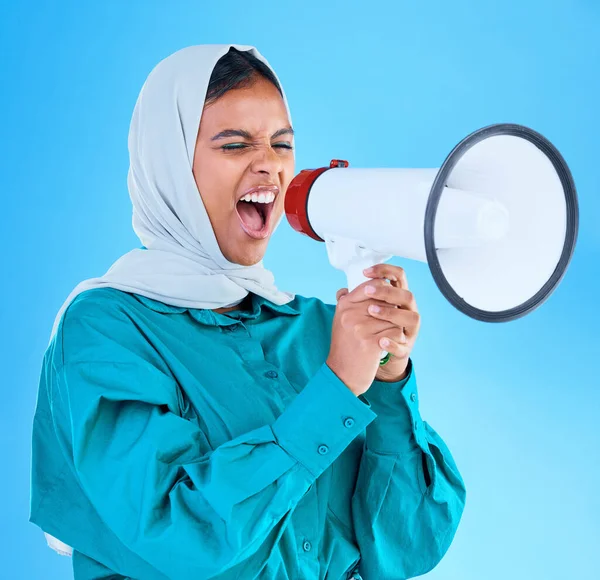 Young woman, muslim and megaphone in studio for protest, human rights and scream by blue background. Girl, islam and loudspeaker for speech, justice and vote for freedom, mission and power politics.