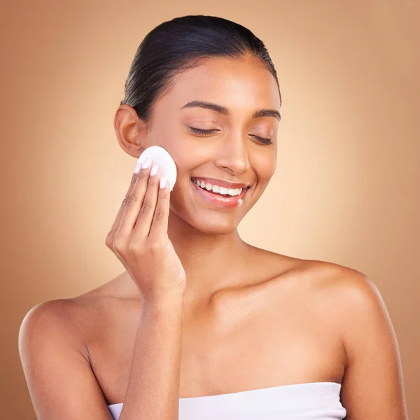 stock image Beauty, skincare and cotton with indian woman and product in studio for self care, makeup remover and cosmetics. Happy, pad and glow with model on brown background for results, natural and facial.