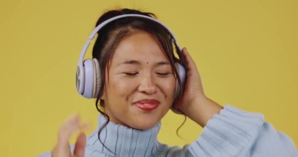 若い女性が音楽やダンスオーディオを聴いているヘッドフォン アジアの女性とスタジオ 笑顔の聴覚とストリーミングラジオや歌を持つGen Z人の幸福 孤立した黄色の背景 — ストック動画