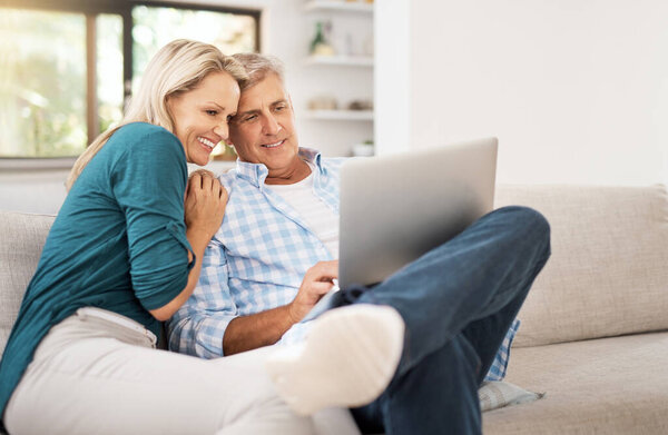 Some downtime. an affectionate mature couple using a laptop while sitting on the sofa together at home