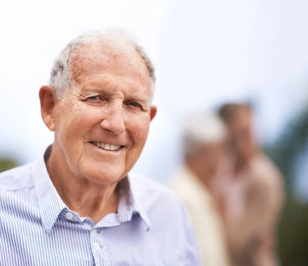 stock image Getting older...but also happier. Portrait of a senior man standing outside with people blurred in the background