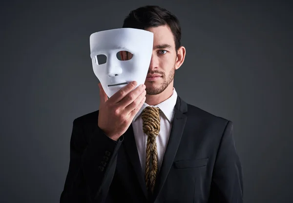 stock image What kind of business practices are lurking beneath. Studio portrait of a young businessman holding a mask in front of his face against a gray background