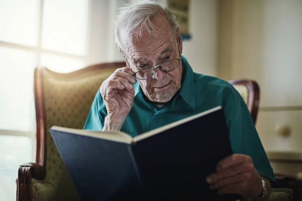 stock image I love myself a good book. a senior man reading a book while relaxing at home