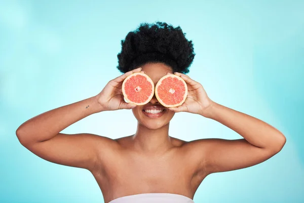 Black woman, face and smile with grapefruit for skincare nutrition, beauty or vitamin C against a blue studio background. Portrait of African female smiling with fruit for natural health and wellness.
