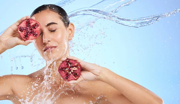 Pomegranate, face and water splash of woman, beauty and wellness on studio blue background. Calm model, shower and healthy fruits for natural benefits, detox vegan nutrition and skincare dermatology.