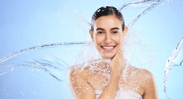 stock image Water splash, portrait and woman shower in studio, blue background and healthy beauty of wellness skincare. Happy female model, wet and cleaning for hygiene, hydration and smile on color backdrop.