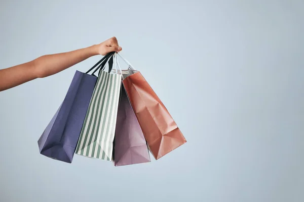 Hands, shopping bags and purchase on studio mockup for fashion, discount or sale against a gray background. Hand of shopper holding bag of gifts, present or luxury retail products on copy space.
