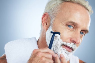 Kıdemli bir adam, tıraş, cilt bakımı ya da sakal ve saç kesimi için stüdyo arka planına karşı kullanılıyor. Tıraş makinesi, krem ya da köpük kozmetik ürünleri kullanan olgun erkek portresi.