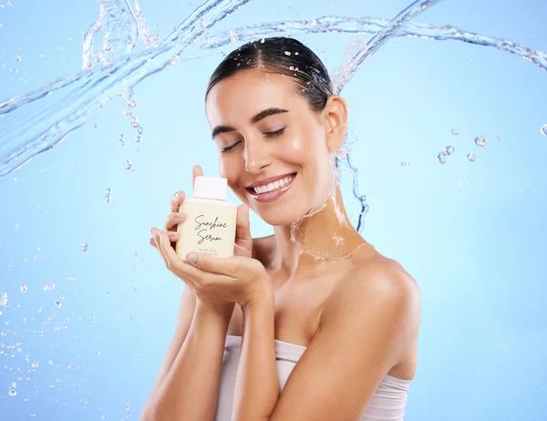 Happy woman, water splash and face with skincare moisturizer, product or cream against blue studio background. Calm female with smile holding lotion or creme for beauty cosmetics or facial treatment.