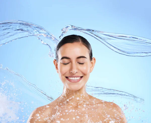 スタジオでの水スプラッシュ 笑顔と女性のクリーニング 青の背景と健康的なスキンケアの美しさ 幸せな女性モデル 湿らせ 衛生のためのシャワー 顔の水分補給と色の背景に顔 — ストック写真