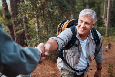 Yardım, el ele tutuşmak, doğa yürüyüşü, tırmanma desteği ve yardım eli uzatmak. Mutlu, birlikte ve dağlarda yürüyüş yapan yaşlı bir adama egzersiz için yardım eden biri..