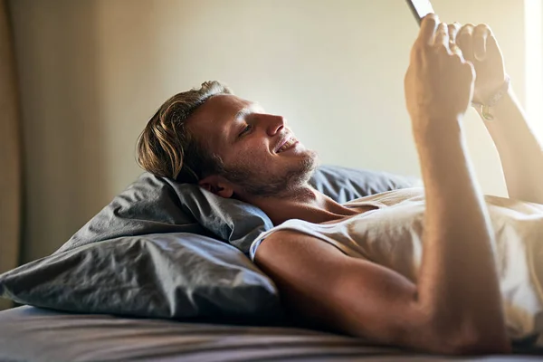 誰もが今週末までに何を見ることができます ベッドに横たわっている間 彼の携帯電話にテキストメッセージを送る若い男 — ストック写真