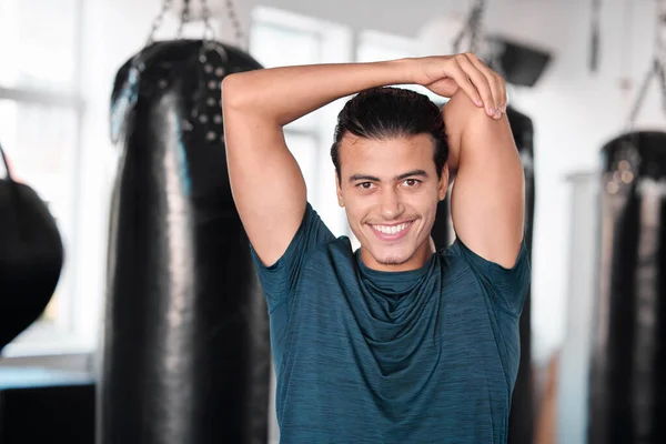 Portrait, stretching arm and man in gym ready to start workout, training or exercise. Sports smile, health fitness and happy male athlete warm up, stretch or prepare for exercising for flexibility