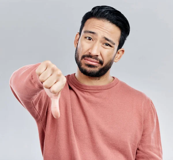 Sad, disappointment and portrait of an Asian man with a thumbs down isolated on a studio background. Review, unhappy and a Chinese guy with a hand sign for a problem, mistake and dislike emoji.