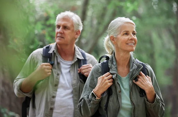 Elderly couple, hiking and active seniors in a forest, happy and relax while walking in nature. Senior, backpacker and woman with man outdoors for travel, freedom and healthy lifestyle in retirement.