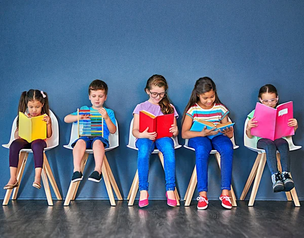 Knowledge is key to growth. Studio shot of a group of kids sitting on chairs and reading books against a blue background