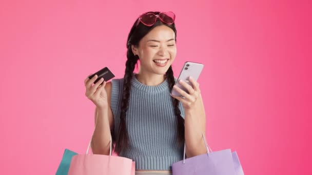 购物通知 电话和兴奋的亚洲女人带着信用卡上网购买衣服 独立的粉色背景和时尚应用程序与一个年轻的 女性和基因Z模型赢得交易 — 图库视频影像