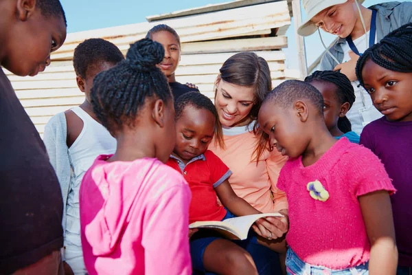 Teaching them how to read. a volunteer worker reading to a group of children at a community outreach event