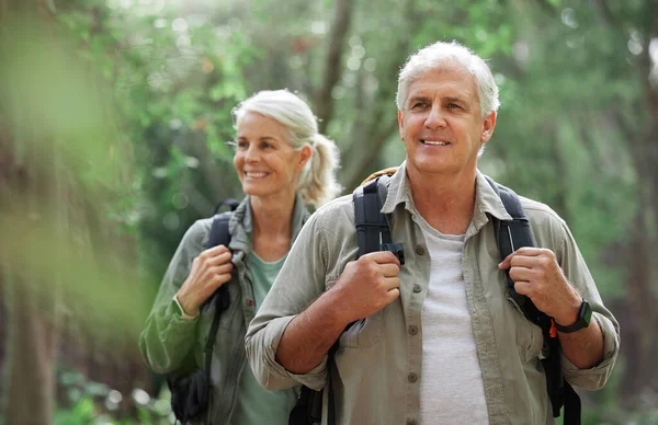 Hiking, elderly couple and active seniors in a forest, happy and relax while walking in nature. Senior, backpacker and woman with man outdoors for travel, freedom and healthy lifestyle in retirement.