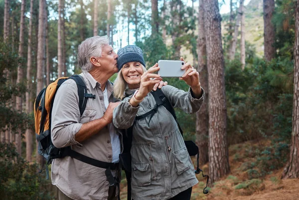 stock image Elderly, couple take selfie and hiking in forest, happy people in nature and memory for social media post. Smile in picture, adventure and fitness, old man and woman are outdoor with active lifestyle.