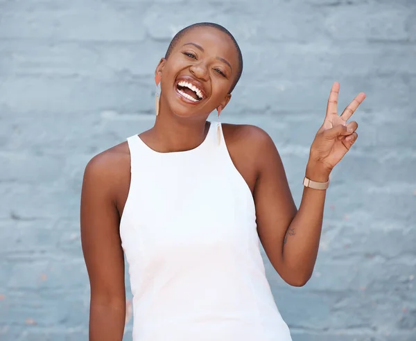 Portrait, hand and peace sign with a business black woman on a blue brick wall with a smile. Hand, emoji and motivation with a female employee showing a v gesture while feeling positive or confident.