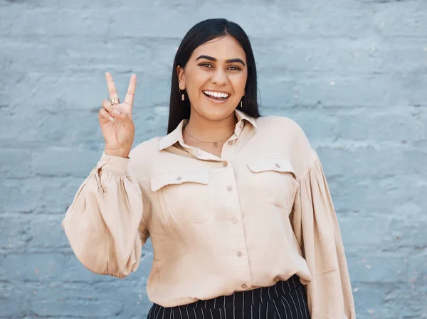 Happy woman, portrait smile and peace sign in business against a gray wall background. Excited and friendly female face smiling showing peaceful hand emoji, sign or gesture with positive attitude.