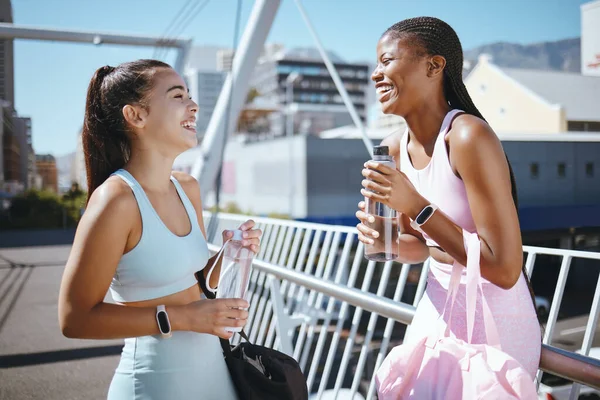 Diversity, fitness and friends laughing while drinking water to hydrate after training, exercise and running outdoors in USA. Smile, healthy and happy black woman enjoys a funny joke with Latino girl.