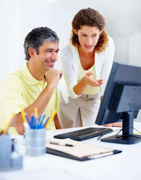 Business colleagues working on computer. Happy business man sitting at table and working on computer with female executive pointing at the screen
