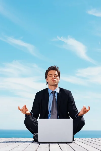 Business man sitting in lotus position with laptop on a pier. Young business man sitting in lotus position with laptop on a pier
