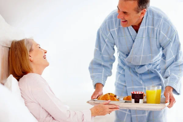 stock image Cheerful mature woman in bed with her husband serving breakfast. Portrait of a cheerful mature woman in bed with her husband serving breakfast