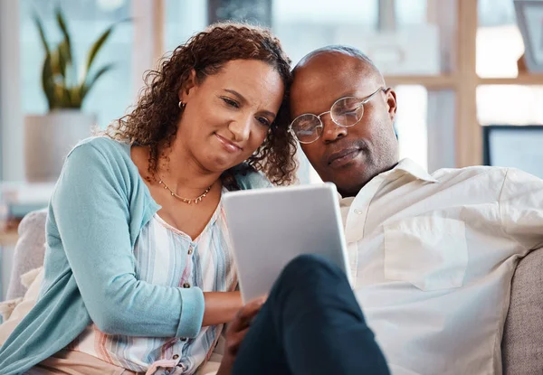 stock image Mature couple, tablet and sofa in home living room for bonding, love and video on app for memory. Black man, woman and mobile touchscreen to watch movie on internet in house on lounge couch to relax.