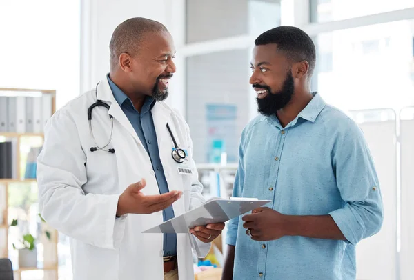 Doctor, black man and patient with clipboard in consultation, talking or health results in hospital. Healthcare, paperwork and happy medical professional with mature person with checklist in clinic