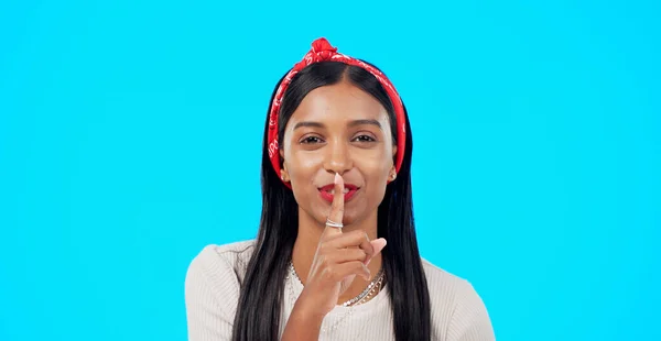 Secret, face and happy woman with finger on lips in studio, blue background and privacy sign. Portrait, indian model and shush for quiet, gossip and whisper of confidential mystery, emoji and smile.