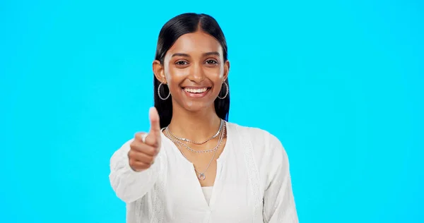 Thumbs up, perfect and portrait of woman with hand gesture for success, approval and isolated in studio blue background. Emoji, face and Indian female with fashion, perfection and support review.