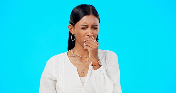 Woman, coughing and sore throat in studio by blue background with medical, health or wellness problem. Young gen z girl, indian model and sick with hand on mouth for cough, healthcare or allergies.