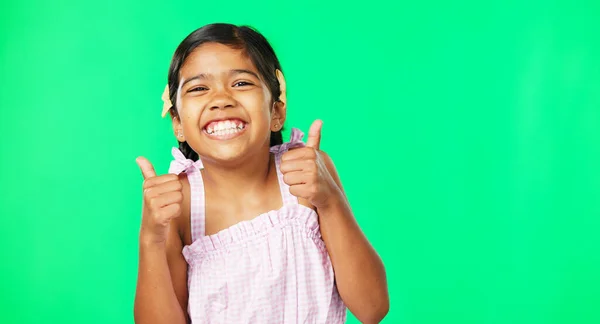 Happy, excited and face of a child with thumbs up on a green screen isolated on a studio background. Success, review and portrait of a girl showing an emoji hand icon for satisfaction and like.
