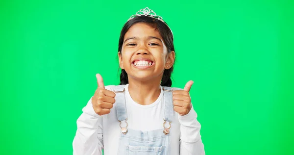 Portrait, children and thumbs up with a girl on a green screen background in studio wearing a princess tiara. Kids, thank you and emoji with an adorable little girl child saying yes in agreement.