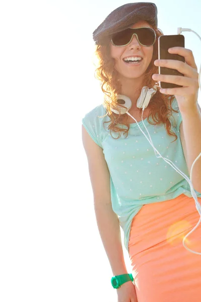 夏天的原声带 一个红头发少女站在外面用她的智能手机选择一个播放列表 — 图库照片