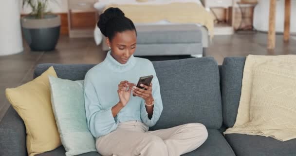 テキストを読んで自宅のリビングルームのソファの上のモバイル 良いニュースと幸せな黒人女性 出会い系アプリ オンライン技術を使用して家のラウンジソファにニューヨークから人のインターネットとWebスクロール — ストック動画