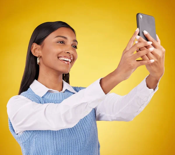 Happy, smile and selfie with woman in studio for social media, technology and internet post. App, online and picture with female on yellow background for happiness, connection and photography.