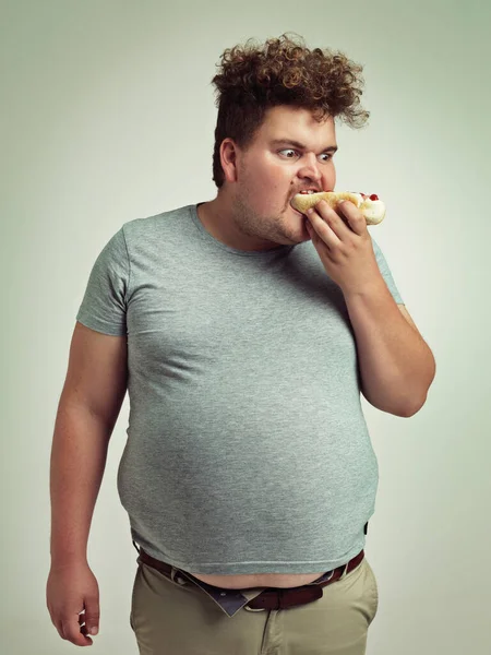 私はこれらのホットドッグを十分に得ることができない スタジオショットのA太りすぎ男食べるAホットドッグ — ストック写真