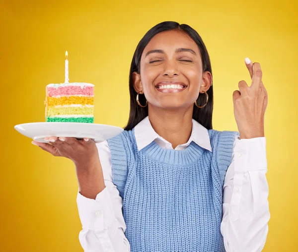 Smile, wish and woman with cake in studio for happy celebration or party on yellow background. Happiness, excited gen z model with fingers crossed and candle in rainbow dessert to celebrate milestone.
