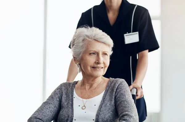 世話をされていることはそのような救済です 車椅子の年配の女性が女性看護師に押されて — ストック写真