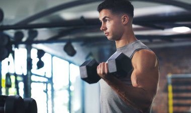 Vücut çalışmanın en zor kısmı kasların olmalı. Spor salonunda dambılla egzersiz yapan genç bir adam.