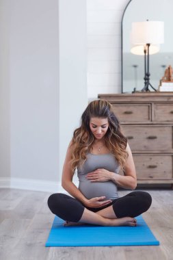 Sağlıklı olmak bebeğinize vermek için en iyi hediyedir. Evde yoga yapan hamile bir genç kadın.