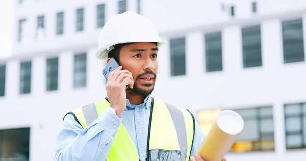 Civil engineer on a phone call while at a construction site discussing a strategy and plan to work on. Close up portrait of confident architect talking with building in the background and copy space.