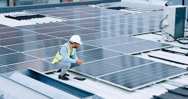Engineer or contractor measuring solar panels on a roof of a building. Engineering technician or electrician installing alternative clean energy equipment and holding a tablet to record measurements.