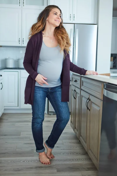 先想清楚一个漂亮的年轻孕妇站在自家厨房里的全景照片 — 图库照片